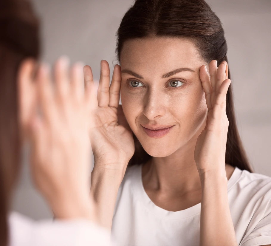 Woman examining her complexion in a mirror with both hands framing her face